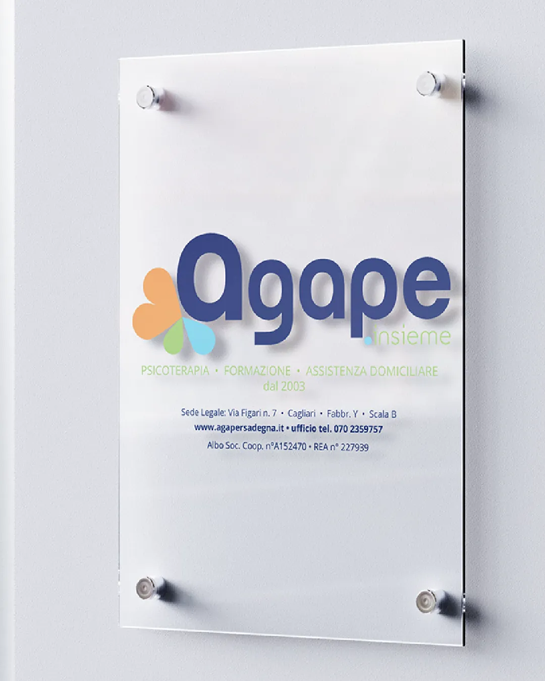 Plaque en verre avec le logo Agape et l’inscription psychothérapie, formation et aide à domicile, fixée à un mur