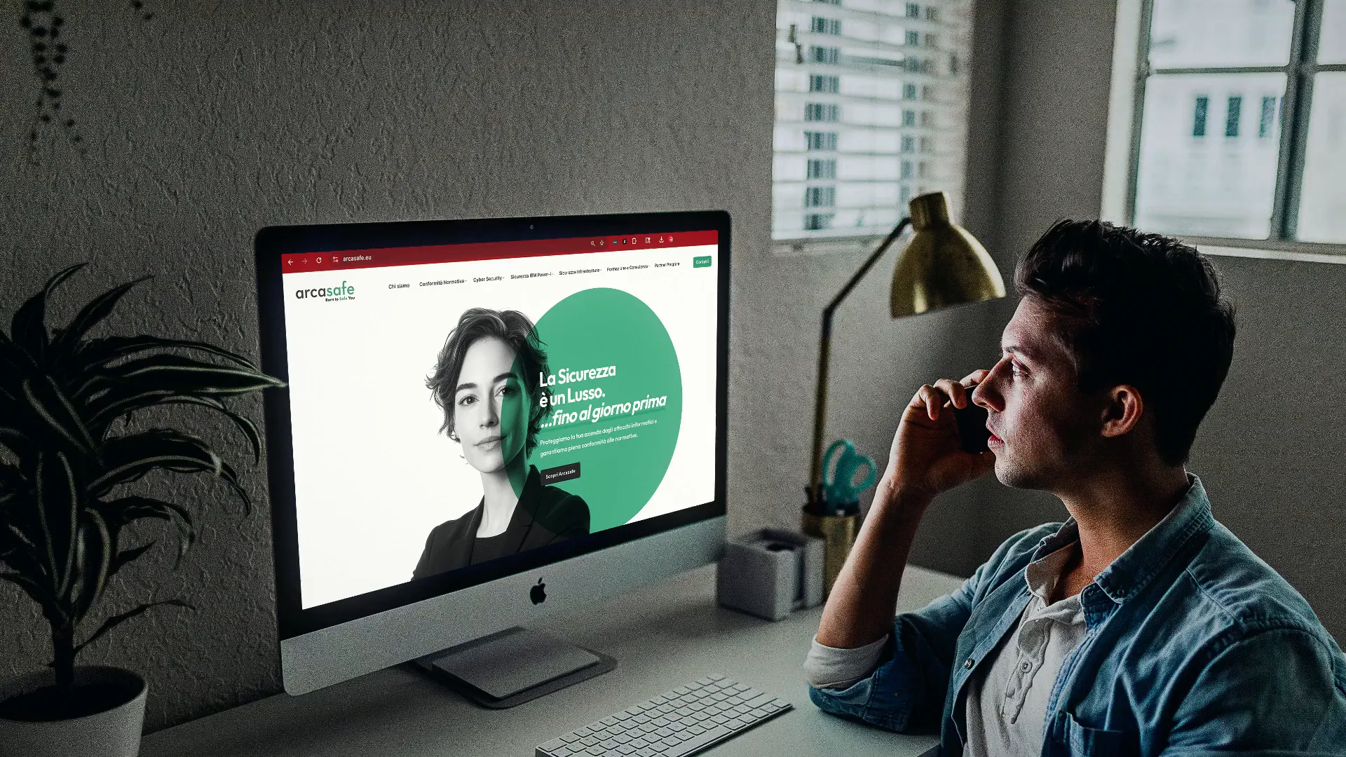 Un homme au téléphone devant un iMac affichant la page d’accueil du site Arcasafe