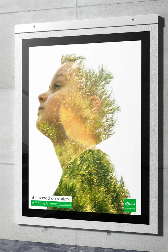 Locandina su un muro di cemento: il profilo di un bambino che guarda in alto, fuso con un pino, con la frase il presente che costruiamo, il futuro che immaginiamo e il marchio Enel Green Power