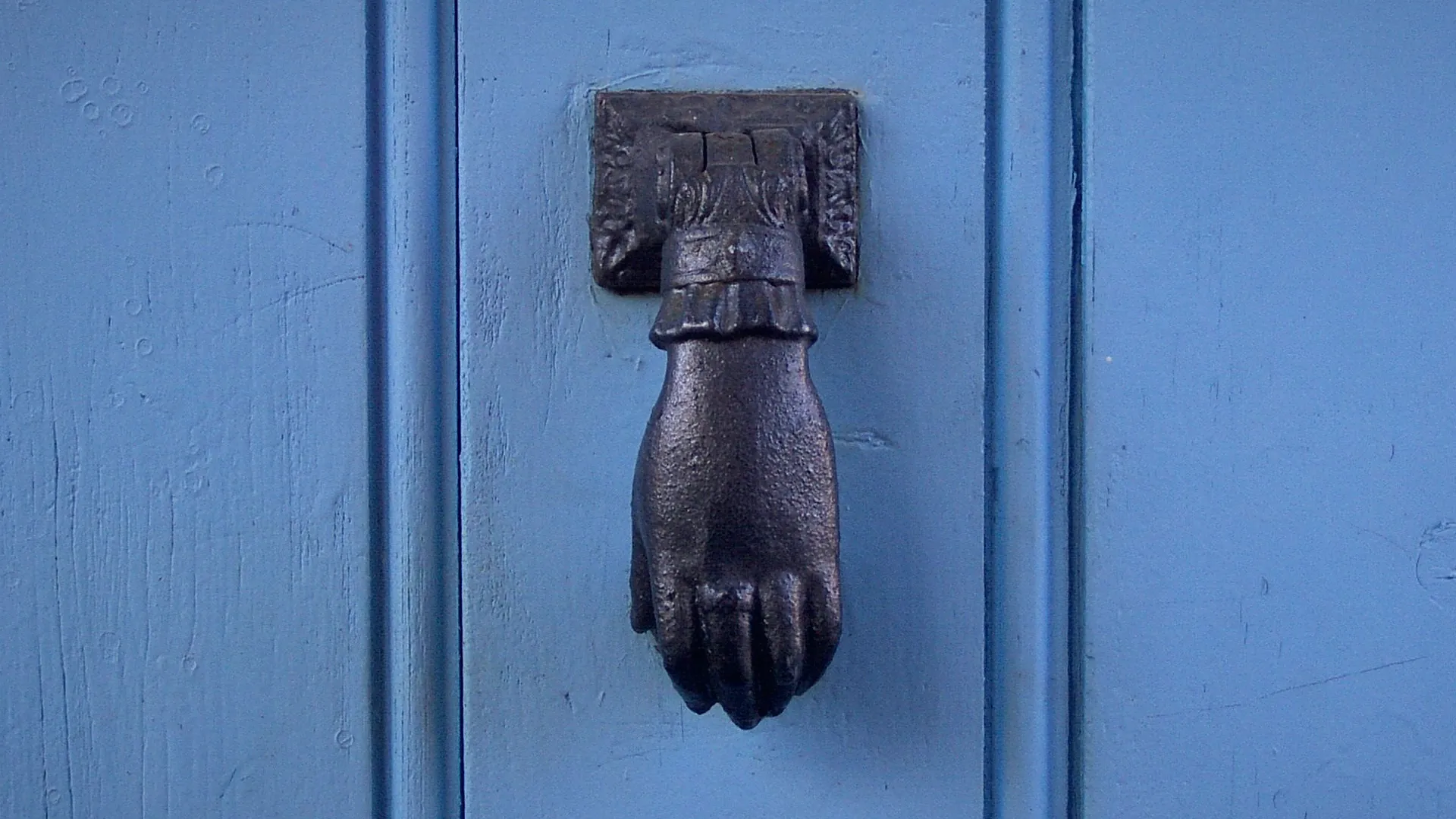 Battiporta in ferro a forma di mano su una porta di legno azzurra
