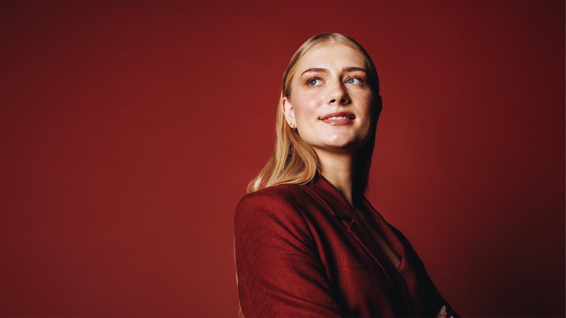 Portrait d’une femme en veste rouge sur fond rouge, le regard tourné vers le haut