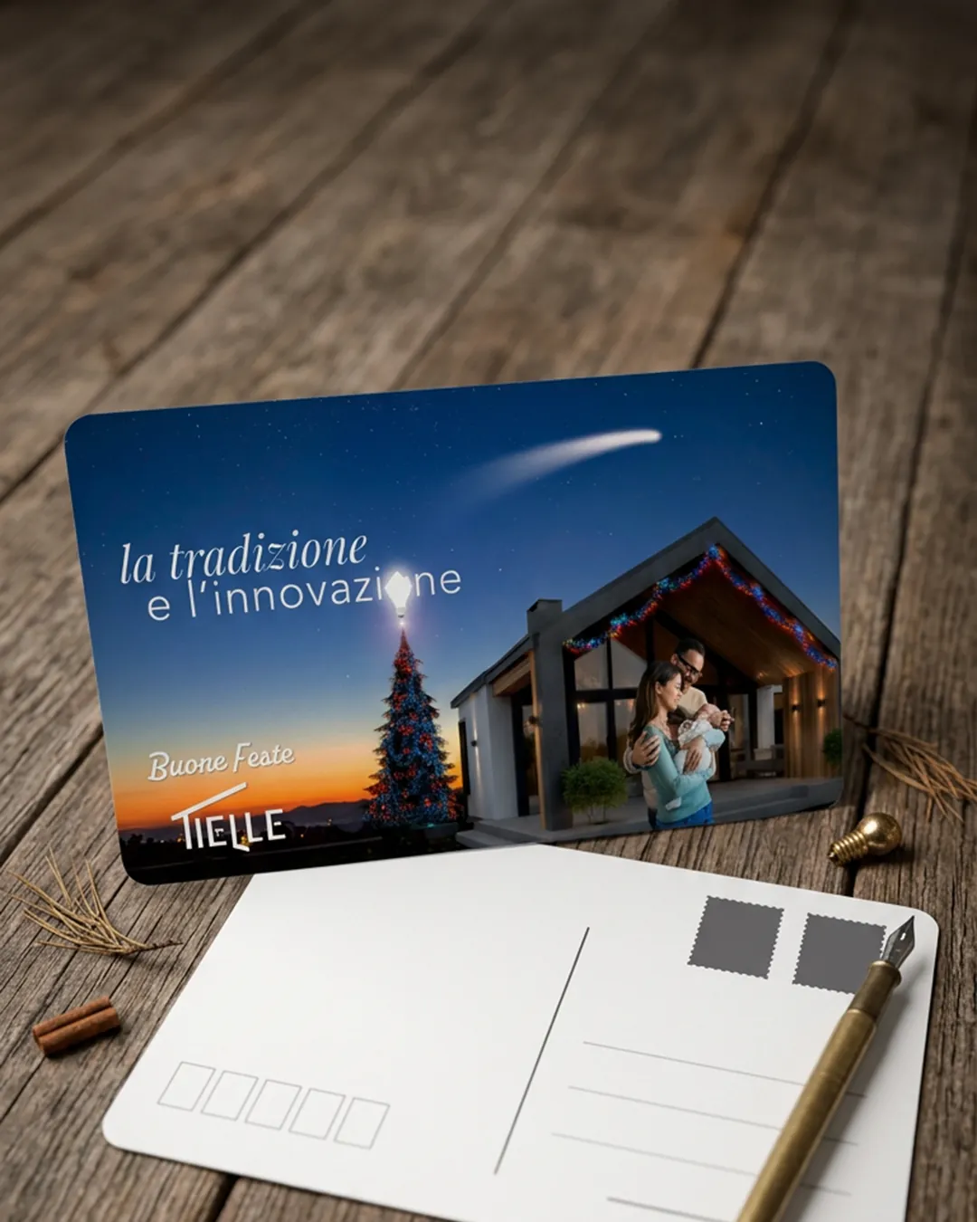 Carte de vœux posée sur une table en bois, appuyée au verso blanc d’une autre carte avec un stylo plume : l’inscription la tradition et l’innovation, un sapin de Noël surmonté d’une ampoule et un couple avec un nourrisson devant une maison